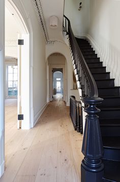 an empty hallway with black railings and wood flooring on the side, along with a staircase leading to another room