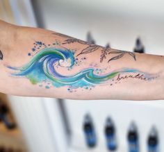 a person's arm with an ocean wave tattoo on it and watercolors