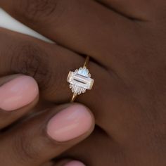 a woman's hand holding a gold ring with an emerald stone in the middle