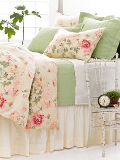 a white bed topped with lots of pillows next to a table and chair near a window