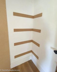 the corner of a room painted white with brown strips on it's walls and wood flooring