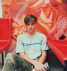 a young man sitting on top of a red bench in front of a colorful wall