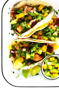 three tacos with avocado, pineapple and cilantro on a white plate