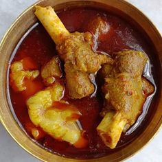 a wooden bowl filled with meat and vegetables covered in red sauce on top of a table