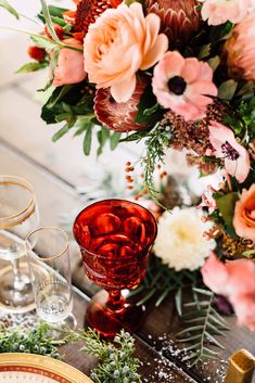 an arrangement of flowers and wine glasses on a table