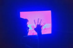 a person holding their hands up in front of a television screen with blue and pink lights