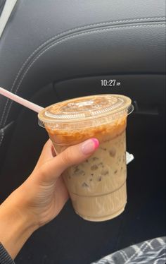 a woman holding up a cup of coffee in the back seat of a car with a straw sticking out of it