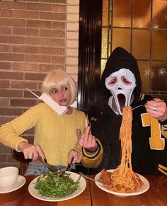 two people in costumes eating spaghetti at a table