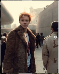 a woman with red hair wearing a fur coat and standing in front of other people