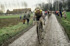 a man riding a bike down a muddy road next to a crowd of people on bikes