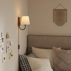 a bed room with a neatly made bed next to a wall mounted lamp and pictures on the wall