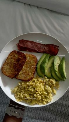 a plate with eggs, bacon, and avocado on it sitting on a bed