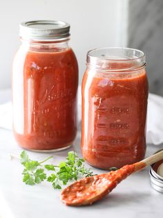 two mason jars filled with red sauce and garnished with parsley next to a spoon