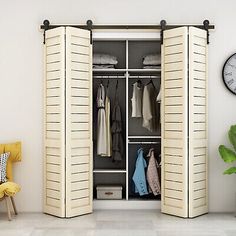 an open closet with clothes hanging on the walls and a clock above it, next to a yellow chair