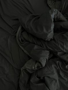 an unmade bed with black sheets and pillows