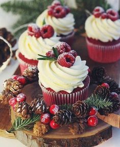 cupcakes with white frosting and berries are on a wooden board next to pine cones