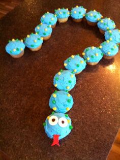 a blue cupcake shaped like a caterpillar with eyes and nose on a table