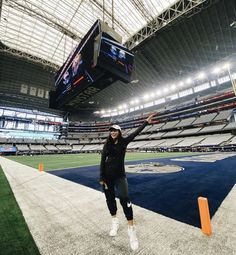 a woman is standing in the middle of an empty football stadium with her arms up