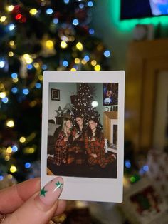 a person holding up a polaroid photo in front of a christmas tree