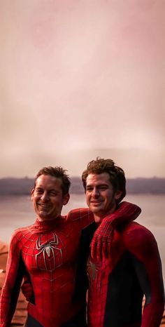 two men dressed as spider - man standing next to each other in front of a body of water