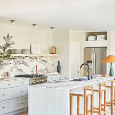 a kitchen with marble counter tops and white cabinets, along with bar stools in front of the island