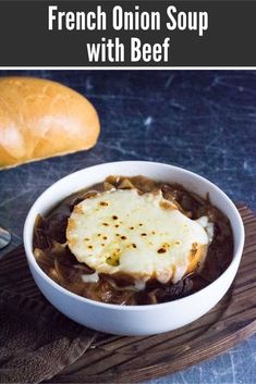 french onion soup with beef in a white bowl on a wooden board next to bread