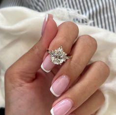 a woman's hand with pink and white manicured nails holding a diamond ring