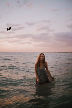 a woman sitting in the water with a bird flying above her and looking at the camera