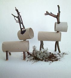 three toilet paper roll sculptures with branches sticking out of them and dirt on the ground