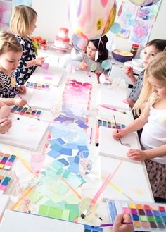 children are painting on paper at a table with balloons and streamers in the background