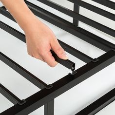 a person is holding the bottom part of a bed frame with metal slats on it