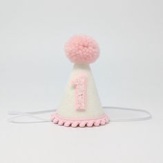 This Listing: Mini 3 inch hat with Pink pom and  trim & Pink glitter birthday number. Size:  Hat measures approximately 3 inches tall and 2 inches wide with an attached comfortable skinny elastic headband meant to be worn around the back of the head. (not under the chin) Adjustable Mini Hats With Round Crown For Birthday, Adjustable Mini Hats With Round Crown For Birthdays, Adjustable Round Crown Mini Hats For Birthday, Playful Mini Hats For Birthday, Playful Adjustable Mini Hats For Birthday, Adjustable Pink Costume Hat For Birthday, Adjustable White Mini Hat For First Birthday, White Adjustable Mini Hats For Birthday, White Adjustable Mini Hat For Birthdays