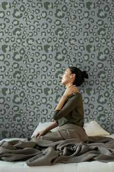 a woman sitting on top of a bed in front of a wallpapered background