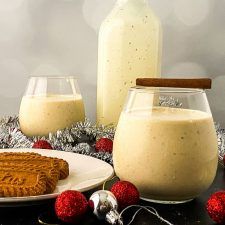 two glasses of milk and some cookies on a table with silver tinsel, christmas decorations and baubles