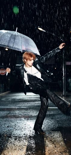 a young man is dancing in the rain holding an umbrella and wearing black leather pants