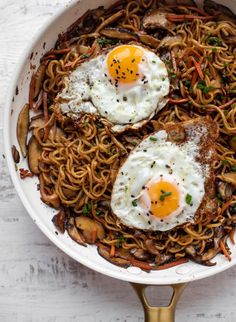 two fried eggs on top of noodles in a skillet with mushrooms and carrots