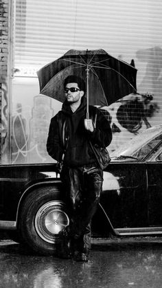 a man holding an umbrella while standing next to a parked car in the rain on a city street