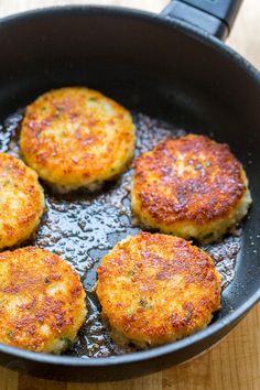 four crab cakes frying in a skillet on a wooden counter top with oil