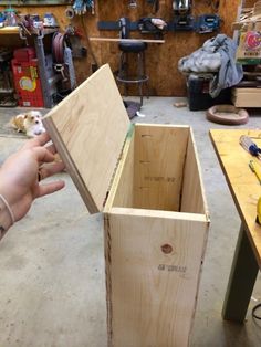 a person holding a wooden box in their hand with tools on the table behind it