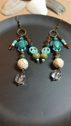 These triple layer earrings are all earth tones with a hippie, boho feel. Many different types of materials and layers for depth.   I used antique bronze findings and ear wires. The circular connector is 12mm wide. I stacked and layered a 15mm dark turquoise stone turtle and 10 mm peace sign charm and beads that consist of brown stone, light brown plastic seed bead, fancy jasper, white seed bead, turquoise stone, green wood, clear bead, 12 mm, 8mm, 7mm, 6mm, 4mm, and 2mm beads. Length of the 3 l Bohemian Drop Earrings With Unique Variations, Green Bohemian Earrings With Unique Variations, Nickel-free Brown Bohemian Earrings, Adjustable Bronze Bohemian Earrings, Hippie Nickel-free Adjustable Earrings, Hippie Adjustable Nickel-free Earrings, Hippie Style Adjustable Nickel-free Earrings, Bohemian Wire Wrapped Bronze Earrings, Bohemian Bronze Wire Wrapped Earrings