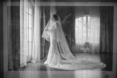 a woman in a wedding dress is standing by a window with her veil pulled back