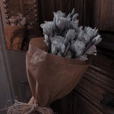 a bouquet of white flowers sitting on top of a wooden doorknob next to a brown paper bag