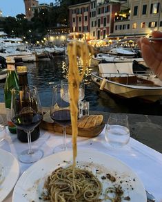 a plate of spaghetti being served at an outdoor table with boats and buildings in the background