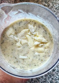 a hand holding a glass bowl filled with broccoli and cheese soup on top of a granite countertop