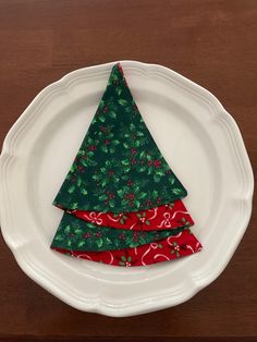 a white plate topped with a green and red christmas tree napkin holder on top of a wooden table