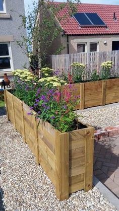 a wooden planter filled with lots of flowers on top of gravel next to a house