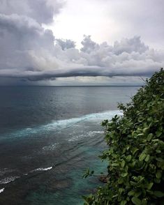 the ocean is very blue and green as it looks out over the water with dark clouds