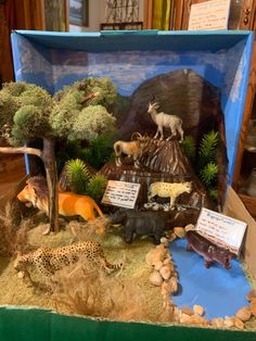 an open cardboard box with fake animals and trees in it's display case on a table