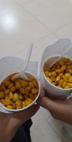 two people holding paper bowls filled with corn