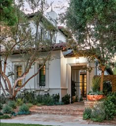 a white house with lots of trees and plants around it's front entrance area